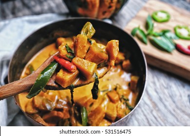 Butternut squash/ pumpkin in authentic Thai red curry coconut sauce with red and green chilies. Serve with grilled cashew nut in a butternut squash bowl. Selective focus at the wooden spoon.