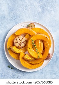 Butternut Squash Slices Baked With Green Thyme Herb And Garlic Clove. Roasted Pumpkin On White Ceramic Plate. Top View, Close Up. Autumn Or Fall Cooking Concept. Blue Background. Thanksgiving Day.