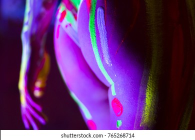 Buttocks of attractive young girl in bright blacklight bodyart glowing in darkness