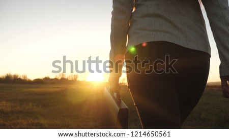 Buttocks of business woman with briefcase in glare of setting sun.