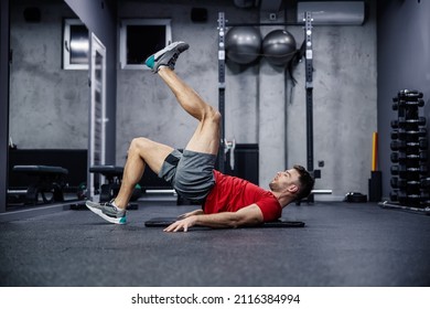 Buttocks And Legs Workout, Muscle Burning And Functional Strength Training. A Young Man In Sportswear Rises To His Heel As He Raises His Other Leg In The Air, Leaning On His Shoulders. Sport, Gym