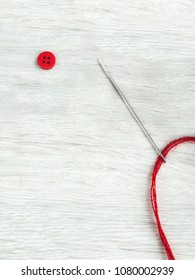 Button, a needle with a red thread on a wooden gray table. Top view. Copy space. Close-up.