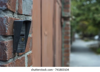 The button on the intercom mounted on the brick wall
