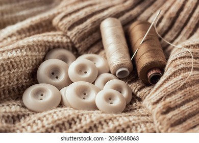 Buttons and a spool of thread with a sewing needle on a beige knitted sweater. Sewing accessories. Copy space.