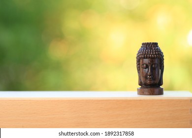 Buudha Head Statue On Wood With Green And Yellow Bokeh Background As Golden Aura. Buddhism Pray For Faith And Asian Religion.