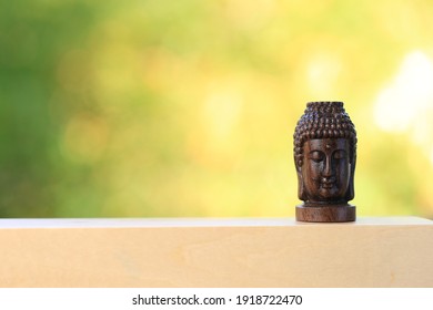 Buudha Head Statue On Wood With Green And Yellow Bokeh Background As Golden Aura. Buddhism Pray For Faith And Asian Religion.