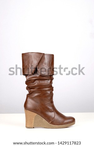 Buy brown leather women's shoes high-heeled boots stands on grey background