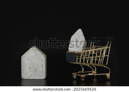 Buy or rent, choice. House model in mini shopping cart on the black background. Buy a house. Concept for property ladder, mortgage and real estate investment. Free space for text, copy space, modern