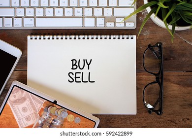 BUY SELL Business Concept Words On Notebook With Tablet Pc, Smartphone, Glasses And Keyboard On Wooden Table