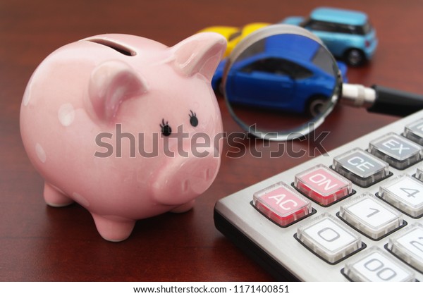 Buy and sell car concept, piggy bank\
with blurred cars, calculator and magnifying\
glass