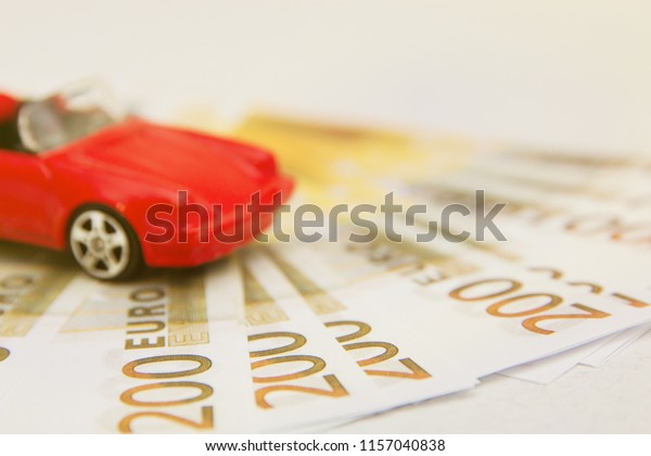 Buy or sell a\
car, rent a car service with a miniature car on a pile of Euro\
banknotes money on a printed\
paper
