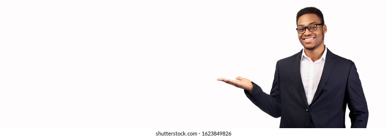 Buy This. Happy afro businessman holding invisible object on his palm, white studio wall, copyspace, panorama - Powered by Shutterstock