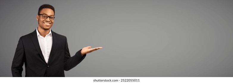 Buy This. Happy afro businessman holding invisible object on his palm, white studio wall, copyspace, panorama - Powered by Shutterstock