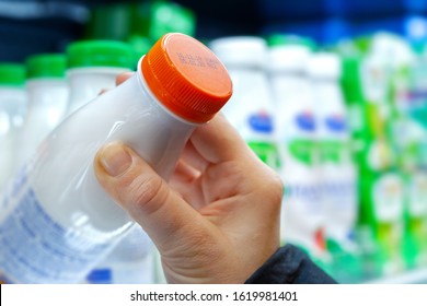 Buyer checks expiration date of dairy product before buying it. Womans hand holding milk bottle in supermarket. Close-up.