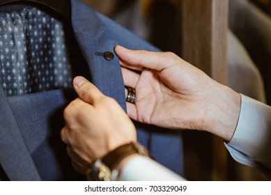 Buyer Holds The Costume Collar Button And Checks The Cloth Of Expensive Clothes In The Clothing Store