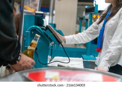 Buyer Pays For A Bottle Of Beer At The Checkout. Cash Register With A Cashier And A Terminal In A Hypermarket. Cashier's Job. Shopping In The Store.