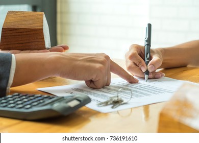Buyers are signing a home purchase agreement from a broker,model house in broker hand and calculator with a house key on the table.