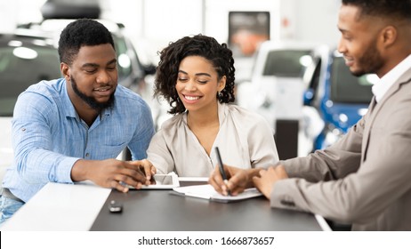 Buying Car. African American Spouses Signing Papers With Auto Seller In Dealership Office. Selective Focus, Panorama