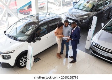 Buying Car. Auto Showroom Manager Consulting Young Black Spouses, Happy African American Couple Purchasing New Auto In Modern Dealership Center, Listening Vehicle Characteristics, Top View Shot