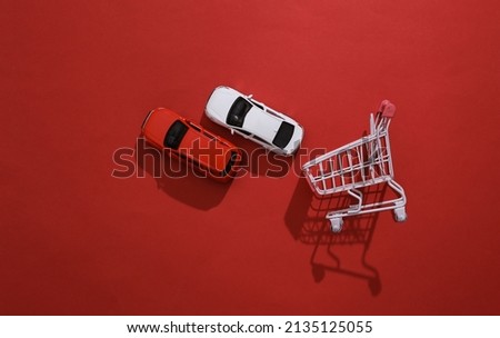 Buying a car concept. Shopping cart and toy cars model on red background