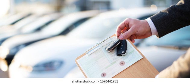 
Buying a car, seller holds registration papers and keys in front of a row of new cars