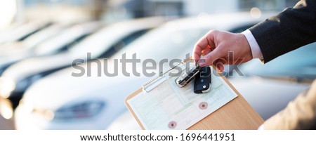 
Buying a car, seller holds registration papers and keys in front of a row of new cars
