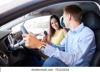 Buying a dream car. Portrait of a beautiful young couple buying a new car at the dealership handsome man laughing and hugging his wife while woman is showing thumbs up - Shutterstock ID 721213216
