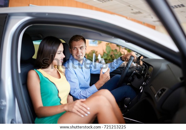 Buying a dream car. Portrait\
of a beautiful young couple buying a new car at the dealership\
handsome man laughing and hugging his wife while woman is showing\
thumbs up