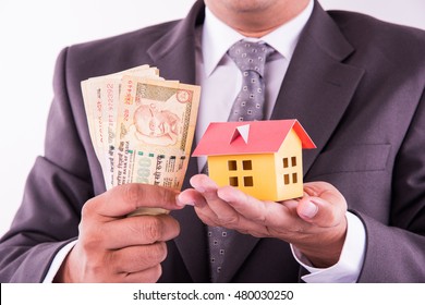 Buying Home Concept, Indian Man Holding Indian Currency Notes In One Hand And Small Model House In Second Hand, Closeup And Selective Focus