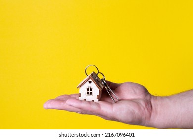 Buying A House. The Buyer Receives The Key To The Property. Mortgage Apartment. Keys And A Small Wooden House In Hand. Handing Over The Keys To The Owner.