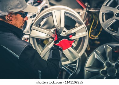 Buying New Alloy Wheels and Seasonal Tires Change Concept Photo. Caucasian Car Service Worker with Large Rim in Hands.