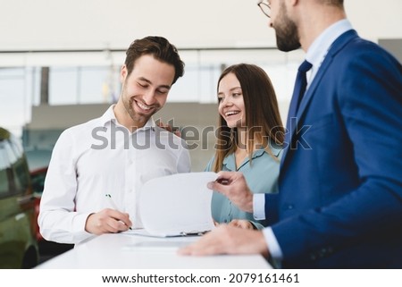 Buying purchasing new car. Male shop assistant congratulating young family couple with buying auto while man signing contract loan mortgage.