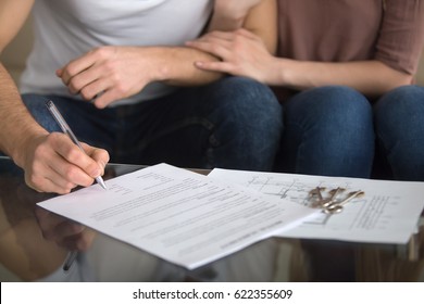 Buying And Renting New Home Concept. Close Up Of Loving Couple Signing Rental Agreement Or Sale Purchase Contract Sitting On Couch Indoors, Starting Family Life, Approved Loan To Buy Real Estate 