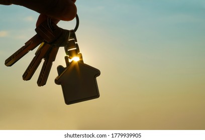 Buying or renting resindental house concept. Man hand holding 3 three silver key with home shape keyring, on sunlight sky cityscapes background. - Powered by Shutterstock