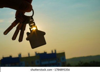 Buying or renting resindental house concept. Man hand holding 3 three silver key with home shape keyring, on sunlight sky cityscapes background. - Powered by Shutterstock