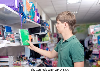  Buying School Supplies At The Supermarket. The Young Man Buys A Notebook In The Store