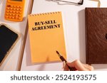 BUY-SELL AGREEMENT text on paper clipboard with chart and notebook on a withe background