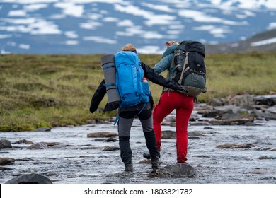By Team Working a Groupe of Hiking Friends Manage to wade across the river with helping hand during long Hike in Padjelanta National Park, northern Europe.