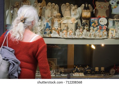 Bydgoszcz, Poland -  August 2017 : Older Woman Looking Through The Window Of A Devotional Articles Shop Selling Angel Figurines