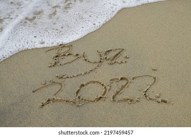 Bye 2022 Text Message Handwritten On Sand Background. Holiday Postcard Template.