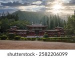 The Byodo In Temple in Oahu, Hawaii, surrounded by greenery, tall pines, and mountain ridges, with a tranquil pond reflecting the serene scene.