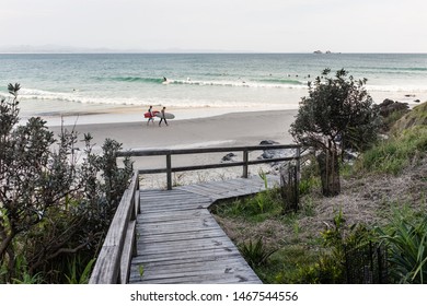 BYRON BAY, AUSTRALIA - SEPTEMBER 20, 2014: Two surfers carrying their surfboards and walking along the shore at Wategos Beach, Byron Bay, NSW, Australia