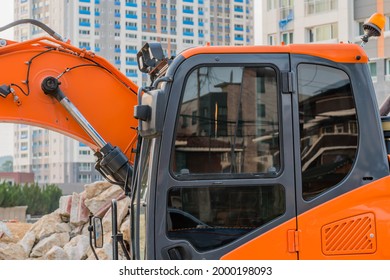 Cab Of Orange Backhoe At Construction Site With Highrise In Background.