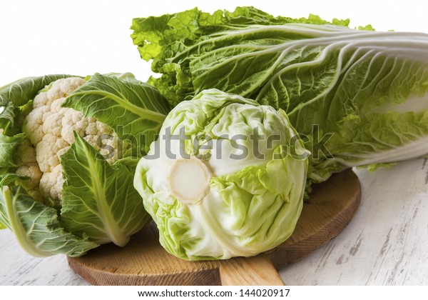 Cabbage family. Cauliflower, chinese cabbage and\
cabbage on wooden cutting board. Bright healthy green vegetable\
background. Healthy summer\
eating.