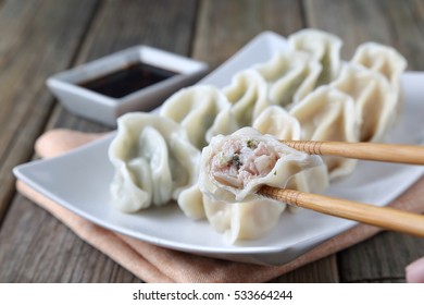 Cabbage Flavor And Chives Flavor Dumplings On A White Plate, With Chili, Garlic, Ginger And Soy Sauce, Wooden Table, Chop Sticks