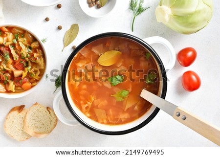 Cabbage soup in cooking pot over white stone background. Top view, flat lay