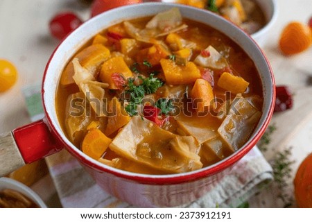 Cabbage soup with pumpkin, carrots and tomatoes in a red pot