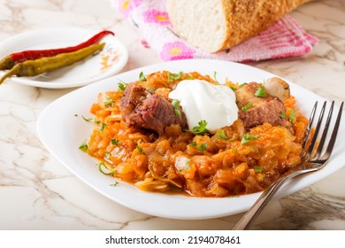 Cabbage Stew With Smoked Pork Ribs, Cream And Green Parsley Served In White Plate With Pickled Chili Peppers And Bread