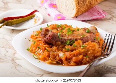 Cabbage Stew With Smoked Pork Ribs And Green Parsley Served In White Plate With Pickled Chili Peppers And Bread