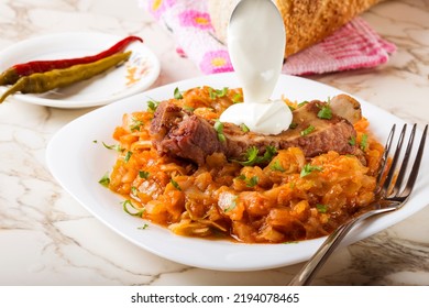 Cabbage Stew With Smoked Pork Ribs, Cream  And Green Parsley Served In White Plate With Pickled Chili Peppers And Bread